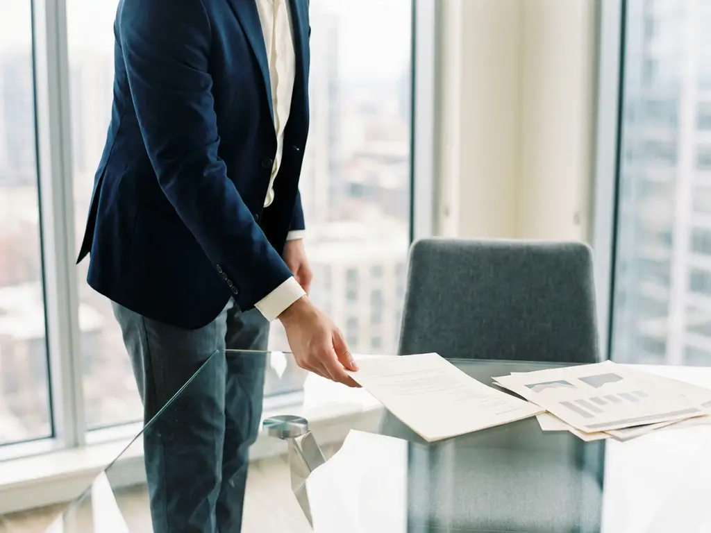 Recruiter sliding a polished resume across a glass desk in a modern office with floor-to-ceiling windows and soft natural light.
