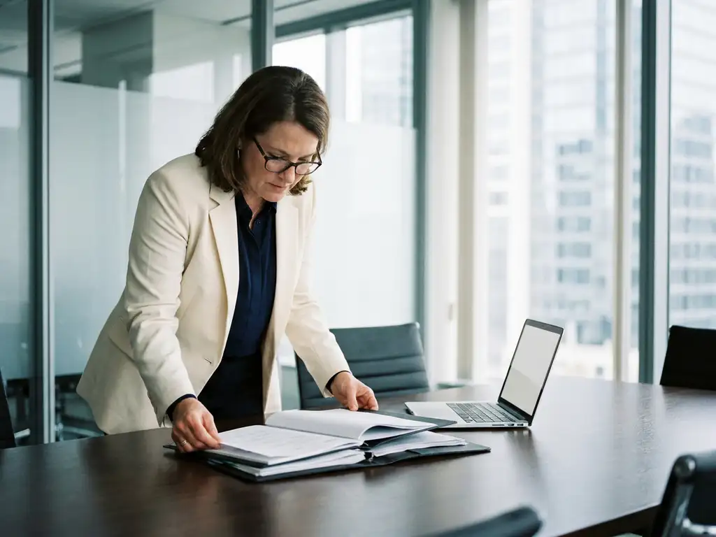 Recruiter reviewing a stack of engineering portfolios and résumés at a polished conference table in a modern glass-walled office.
