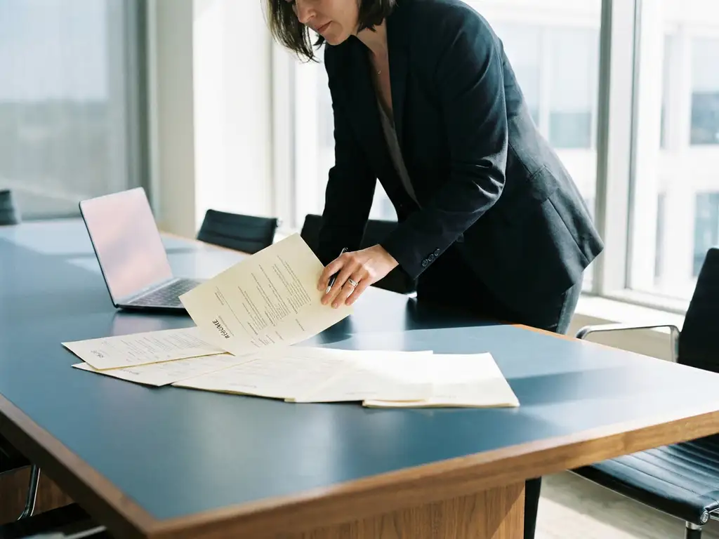 Recruiter reviewing a standout résumé among candidate profiles on a conference table, laptop glowing nearby, modern office with natural daylight.